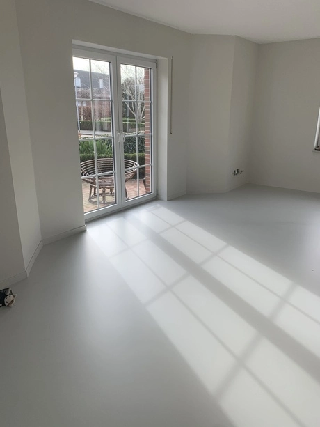 gegoten vloer reflecteert zonlicht bij openslaande deuren